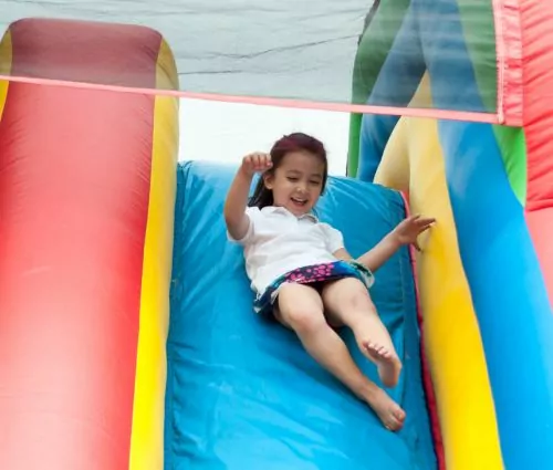 Girl laughing, sliding down blue inflatable slide rental from Jumptastic